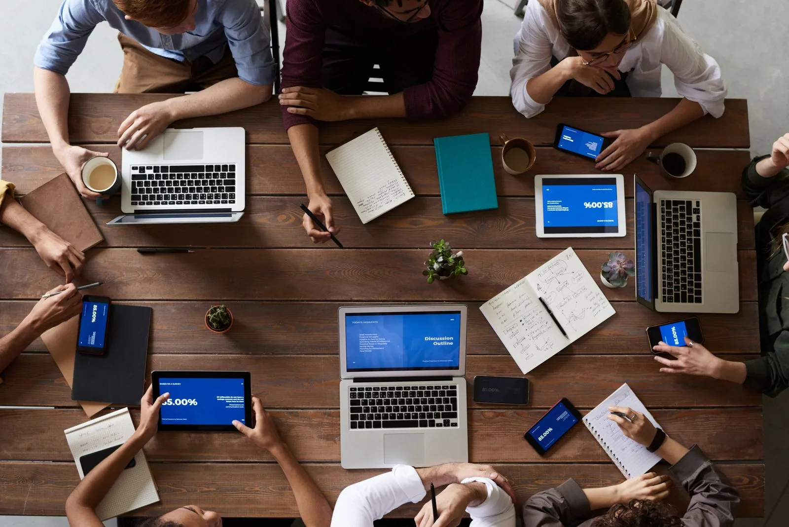 Equipe de escritório trabalhando em volta de uma mesa com notebooks, tablets e cadernos